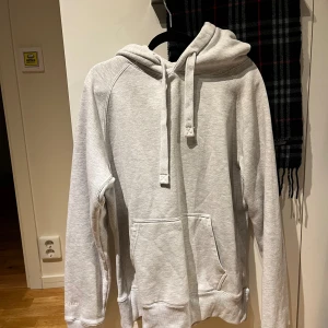Ljusgrå hoodie från Russemerch, M - Ljusgrå hoodie från Russemerch i mjuk bomullsblandning. Klassisk modell med huva, snörning och stor magficka. Långärmad och ribbade muddar vid ärmslut och nederkant. Perfekt för chill dagar eller när du vill vara extra bekväm.