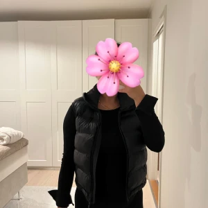 Svart dunväst från Zara - Snygg svart dunväst från Zara med hög krage och dragkedja framtill. Västen är quiltad och har en klassisk, stilren look som passar perfekt till lager-på-lager. Enkel att matcha och superbekväm för kyligare dagar. Den är helt ny