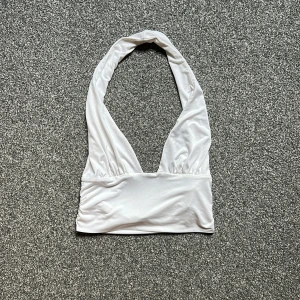 Vit halterneck linnetopp - Snygg vit halterneck linnetopp med djup v-ringning och bred resår under bysten. Toppen är ärmlös och har en stilren, minimalistisk look som passar perfekt till sommarens outfits.