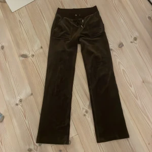 Bruna Juicy Couture - Mörkbruna från Juicy Couture med bred resår i midjan och snörning. Byxorna har raka ben, framfickor och bakfickor och silverfärgade knappar. 