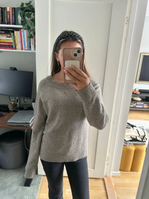 Beige stickad tröja från Vero Moda - Mysig grå stickad tröja från Vero Moda med rund halsringning och långa ärmar. Tröjan har en enkel och stilren design med ribbade muddar vid ärmslut och nederkant. Perfekt att slänga på sig när det är kyligt ute.