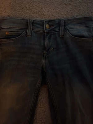 Mörkblå bootcut jeans  - Säljer ett par mörkblå jeans från weekday med utsvängda ben. Lite slitningar längst ner på byxan men inget man lägger märke till. Midjemått rakt över 37 & innerbenslängd är 74