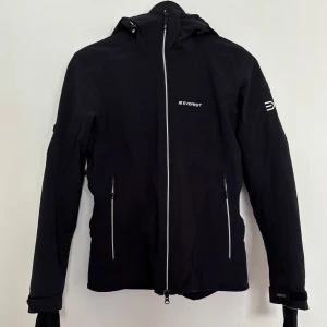 Svart vindjacka från Everest strl 36 - Skidjacka från Everest. Fint skick, sparsamt använd. Har snölås och många fickor. Har även recco-system för räddning. Hämtas eller skickas mot frakt. Storlek 36/s. Säljes då den inte passar mig längre.