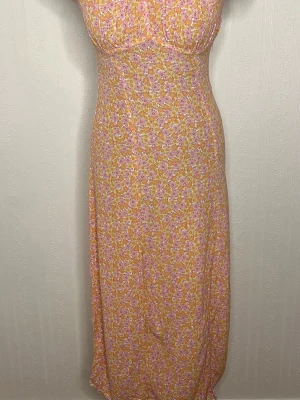 Blommig långklänning i pastellfärger - Supersöt långklänning med småblommigt mönster i rosa, gul och vit. Klänningen har korta puffärmar med volangkant och smockad överdel som ger en fin passform. Perfekt för sommarens alla tillfällen! Använd en gång 