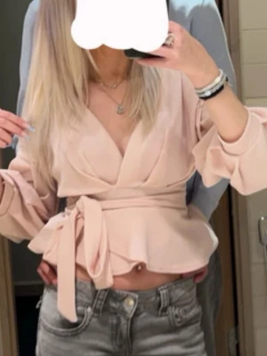 Ljusrosa omlottblus med knytband - Supersnygg ljusrosa omlottblus med breda ballongärmar och knytband i midjan. Blusen har v-ringad urringning och volangkant nedtill som ger en feminin look. Perfekt till jeans eller kjol för en trendig outfit.