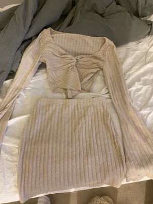 Beige ribbat set med knyt - Säljer ett beige ribbat set med långärmad croppad topp och knyt framtill samt matchande kjol. Materialet är mjukt och skönt. Ärmarna är långa och lätt utsvängda. Från shein.