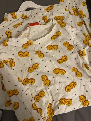 Pyjamas med lussebullar-mönster - Unika vita byxor med ett lekfullt mönster av gula lussebullar och små bruna stjärnor. Byxorna har resår i midjan storleken är M men passar också S