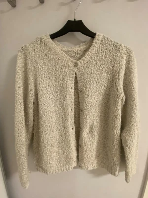 Beige glittrig kofta med knappar - Mysig beige kofta med glittriga inslag och knappar framtill. Koftan är stickad med en fluffig struktur och har lång ärm. Går att styles på flera olika sätt och passar till de mesta! Har tyvärr klippt bort lappen men skulle säga att storleken är S, funkar dock för mindre och större också!! Tror att märket är lindex men inte säker😅