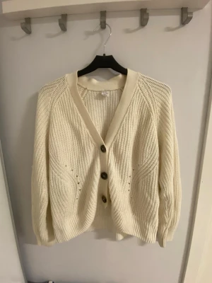 Beige stickad kofta - Säljer en beige stickad kofta med snygg struktur och tre stora knappar framtill. Koftan har v-ringning, lång ärm och ribbade muddar. 