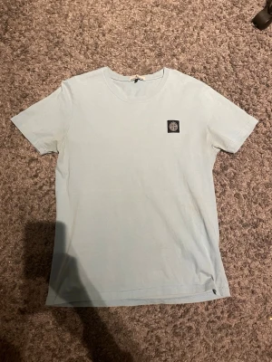 Ljusblå Stone Island t-shirt - Snygg ljusblå t-shirt från Stone Island. Den är i bra skick men är lite ur tvättad. Den har lite små hål i ryggen men är inte så synliga.