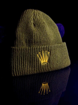 MoneyCrown Mössa - MoneyCrown-mössan är en stilren och självsäker mössa i olivgrön ton med broderad guldkrona framtill. Tillverkad i mjukt och värmande stickat material som sitter bekvämt hela dagen. En perfekt accessoar för dig som vill kombinera streetstyle med lyxig attityd. Funkar lika bra till vardags som för att lyfta en clean outfit. Helt ny.