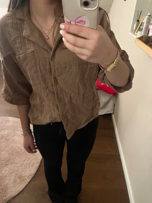 Brun skjorta i bomull med knappar - Säljer en brun skjorta i mjuk och luftig bomull med trekvartsärm och klassisk krage. Skjortan har knappar framtill och en bröstficka. Perfekt till jeans eller kjol för en chill look.