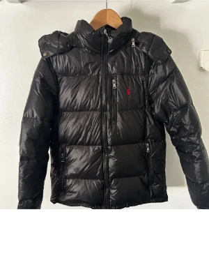 Svart pufferjacka från Polo Ralph Lauren - Svart glossy puffer jacka från Polo Ralph Lauren i storlek S. Väldigt bra skick, använd under December-Januari. NYPRIS: 5600kr, MITT PRIS: 2399kr. Priset är ej hugget i sten. Hör gärna av dig vid frågor!😊