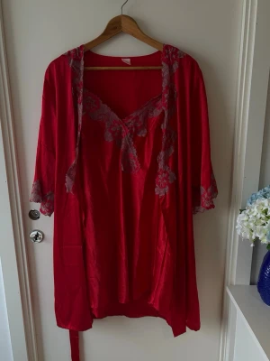 Röd lingerie set med spetsdetaljer - Röd natlinne / klänning och  kimono med vackra spetsdetaljer i grått längs kanterna och ärmsluten. Kimonon har ett bälte i midjan och v-ringad hals. Perfekt för dig som vill ha något extra snyggt och bekvämt hemma. Storlek XL, passar M-XL 
