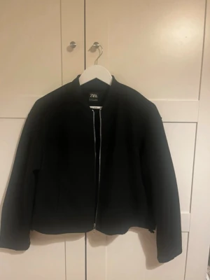 Svart bomberjacka från Zara - Säljer en svart bomberjacka från Zara med klassisk rak passform och silverfärgad dragkedja framtill. Jackan har lång ärm och enkel, stilren design som funkar till det mesta. Perfekt för dig som gillar en clean look och vill ha något som är lätt att matcha.