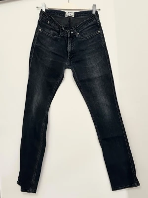 Svarta slim  jeans från Acne Studios - Snygga svarta slim jeans från Acne Studios med klassisk femficksdesign. Jeansen har en mörk tvätt med lätt slitning och raka sömmar. Ett lagat hål i skrevet hos skräddare, något slitna. Size 30/32.