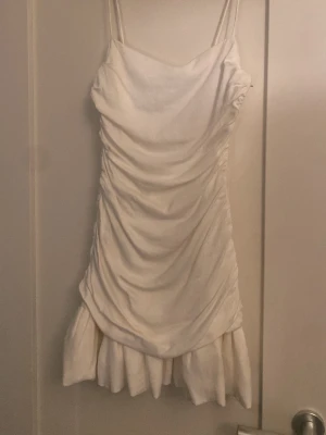 Vit kortklänning med volang - Supersöt vit kortklänning med tunna axelband och draperad effekt längs sidorna. Klänningen har en volangkant nedtill och dragkedja i sidan för enkel påklädning. Perfekt för sommarens alla tillfällen, drömklänning på skolavslutningar eller midsommar. Bortklippt etikett men från Zara💕