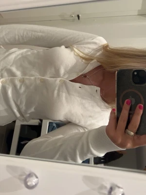 Vit kofta med knappar - Säljer en klassisk vit kofta med rund hals och knäppning framtill. Tröjan har långa ärmar och ribbade muddar vid ärmslut och nederkant. Perfekt att slänga över en topp eller bära stängd för en clean look. Prislapp finns kvar, aldrig använd!