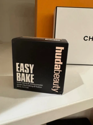 Huda Beauty Easy Bake Cupcake puder - Löspuder Easy Bake från Huda Beauty i nyansen Cupcake. Kommer i en svart förpackning med beige text och innehåller 20 g. Perfekt för att sätta sminket och få en matt finish. Pudret är lätt och ger en mjuk look.