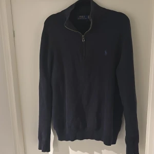 Mörkblå stickad tröja Polo Ralph Lauren - Mörkblå stickad tröja från Polo Ralph Lauren med halv dragkedja och broderad logga på bröstet. Tröjan har lång ärm och klassisk passform, perfekt för lager-på-lager. Materialet är mjukt och ger en stilren look. Väldigt bra skick. Nypris: 2300kr