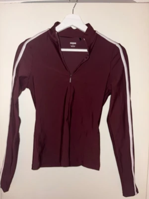 Träningsset från stronger - Säljer ett par vinröda leggings från Stronger med vita ränder längs sidan med tillhörande överdel. De är tillverkade i ett stretchigt syntetmaterial som passar perfekt för träning. Tight passform och hög midja för en snygg och bekväm look.