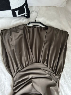 Kakigrön klänning med drapering - Säljer en elegant kakigrön klänning med djup v-ringning och snygg drapering längs hela klänningen. Klänningen är ärmlös och har ett mjukt, glansigt tyg. Klänningen är ifrån Zara och är i storlek S. Har endast använts en gång. 