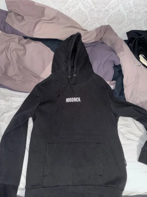 Hoodrich hoodie - Svart hoodie från Hoodrich med vit logga på bröstet. Klassisk modell med huva och snörning samt stor magficka framtill. Perfekt för dig som gillar streetwear och vill ha en enkel men snygg look. Fraktas endast och köparen står för frakt.