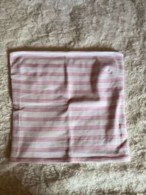 Randig bandeau tubtopp Gina Tricot - Säljer en söt bandeau tubtopp från Gina Tricot i vitt med ljusrosa ränder. Toppen är axelbandslös och har en rak, tight passform. Perfekt till sommaren och enkel att matcha med shorts eller kjol.