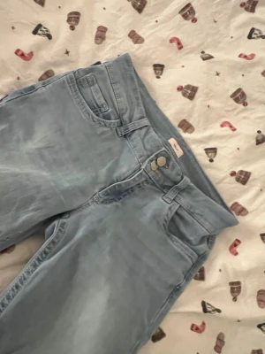 Bootcut ljusblå jeans med broderi - Snygga ljusblå bootcut jeans från Wrangler med klassisk femficksdesign och broderad detalj i rött på bakfickorna. Jeansen har hög midja och är tillverkade i mjukt denimtyg som ger en skön passform. Perfekta för dig som gillar retrovibbar och avslappnad stil. Jag har sytt upp de lite men de är ändå lite långa på mig som är 162cm💓jag köpte fel storlek därför säljer jag😊Nypris 699kr och jeansen har inte kommit till användning så mycket därför säljer jag ändå lite dyrt💕