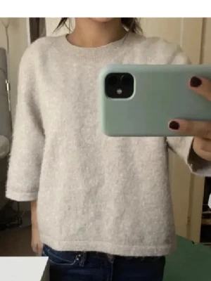 Beige stickad tröja med trekvartsärm - Mysig beige stickad tröja med rund halsringning och trekvartsärm. Tröjan har en rak, något boxig passform och är perfekt för lager på lager. Enkel och stilren design som passar till det mesta.