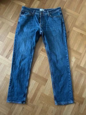 Blå jeans från Jack & Jones - Säljer dessa blå jeans från Jack & Jones med raka ben och femficksmodell åt min brorsa . Jeansen har normal passform, bälteshällor och knappgylf. Tillverkade i slitstarkt denim med snygga kontrastsömmar och diskret bakficka med broderad detalj. Skriv vid frågor!