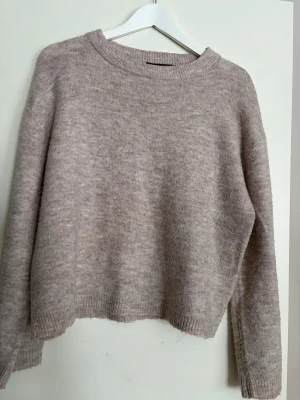 Beige stickad tröja  - Mysig beige stickad tröja med rund hals och långa ärmar. Tröjan har en relaxed passform och ribbade muddar vid ärmslut och nederkant. Perfekt för lager på lager under kyliga dagar.