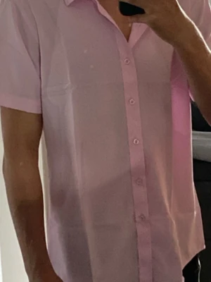 Ljusrosa kortärmad skjorta - Säljer en ljusrosa skjorta med korta ärmar och klassisk krage. Skjortan har knappar hela vägen framtill och är gjord i ett tunt, mjukt bomullstyg. Perfekt för dig som vill ha en clean och stilren look med lite färg. Storleken är S-M 