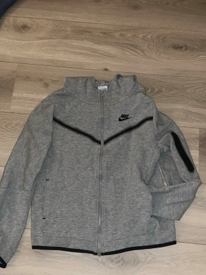 Grå Nike tech hoodie - Säljer denna snygga gråa zip hoodie från Nike. Finns inga synliga defekter på den och den är inte så använd. Funkar bra till vardags. Bara att skriva vid frågor