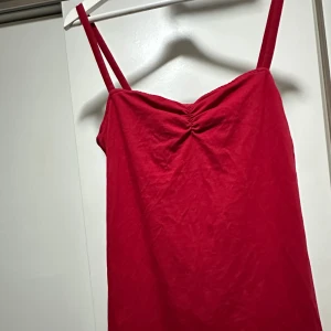 Röd kort klänning från Divided - Snygg röd klänning från Divided med smala axelband och rynkdetalj vid bysten. Modellen är rak och kort, perfekt för dig som gillar enkel men trendig stil. Tillverkad i mjuk bomull som känns skön mot huden.