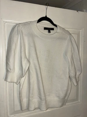 Vit stickad tröja med puffärm Vero Moda - Supersöt vit stickad tröja från Vero Moda med puffiga korta ärmar och ribbade muddar. Perfekt till både jeans och kjol för en clean look. Rund halsringning och mjukt material som känns skönt mot huden.
