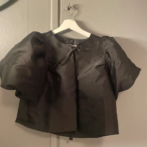 Svart blus med puffärm från Gina Tricot - Säljer en svart blus från Gina Tricot i storlek S. Blusen har stora puffärmar och en söt knyt-detalj vid halsen. Materialet har en lätt glansig finish som ger en lyxig känsla. Perfekt för dig som gillar statement-ärmar och stilrena detaljer.