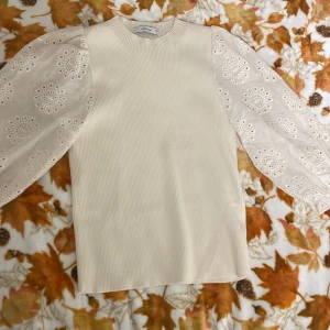 Vit blus med broderade puffärmar Reserved - Supersöt vit blus från Reserved med ribbad kropp och transparenta puffärmar i broderad bomull. Ärmarna har fina cirkelbroderier och avslutas med resår vid handleden. Perfekt för dig som gillar unika detaljer och romantisk stil.