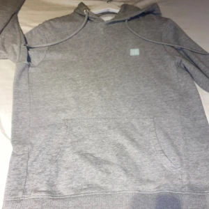 Grå hoodie från Les Deux - Säljer en stilren grå hoodie från Les Deux med klassisk huva och dragsnören. Tröjan har en liten logga på bröstet och en stor magficka framtill. Tillverkad i mjuk bomull, perfekt för chill dagar eller när du vill ha en clean look.