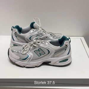 Vita New Balance 530 sneakers - Säljer ett par vita New Balance 530 sneakers med gröna detaljer och meshpaneler. Skorna har snörning, platt sula och den klassiska N-loggan på sidan. Perfekta för dig som gillar sportig och retro stil.