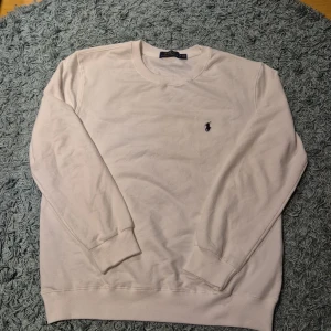 Vit sweatshirt från Polo Ralph Lauren - Säljer en stilren vit sweatshirt från Polo Ralph Lauren i storlek M men passar som en S. Tröjan har långärmad design, rund hals och den klassiska broderade loggan på bröstet. Tillverkad i mjuk bomull med ribbade muddar vid ärmslut och nederkant. Perfekt för en clean och enkel look. Ny pris 1200 aldrig använd