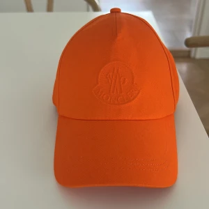 Orange keps från Moncler - Snygg orange keps från Moncler med broderad logga framtill i samma färg. Klassisk baseballmodell med justerbar rem bak med Moncler-logga. Tillverkad i bomull för skön passform och cool look. Nypris ca 1600 kr.