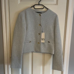 Ljusblå kavaj från Zara XS - Snygg ljusblå kavaj från Zara i storlek XS., guldfärgade knappar framtill och vid fickorna, samt ett diskret melerat mönster. Materialet är mjukt och känns lyxigt, perfekt för att lyfta din outfit. Fodrad insida och klassisk krage.
