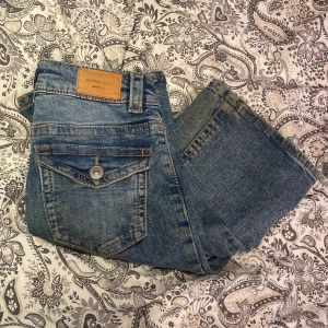 Blå bootcut jeans från Gina Tricot - Snygga blå jeans från Gina Tricot, modell Perfect Jeans. Klassisk femficksdesign med cool knappdetalj på bakfickan och bootcut-ben. Jeansen har normal passform och är tillverkade i mjukt denimtyg med snygg tvätt.