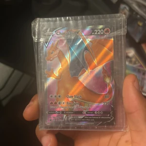 Charizard V Pokémonkort - Snyggt Charizard V-kort med holografisk effekt, perfekt för samlare och Pokémon-fans! Kortet har 220 HP och coola attacker som Claw Slash och Fire Spin. Skyddat i plastficka, redo att boosta din samling eller spel. Ett måste för dig som älskar Pokémon!