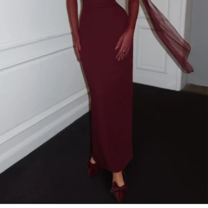 Vinröd långklänning med scarfdetalj - Säljer en helt ny, oanvänd klänning med alla taggar på! Ordinarie pris: 1321 kr (1500 kr inkl. frakt). Klänningen är liten i storlek- enligt hemsidan rekommenderas att gå upp en storlek. Köpt för att användas till ett bröllop som tyvärr blev inställt, så den har aldrig kommit till användning.