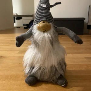 Randig tomte i mjukt tyg - Säljer en lång, randig tomte i grått och vitt med böjd topp. Tillverkad i mjukt tyg, perfekt för julens dekorationer. 