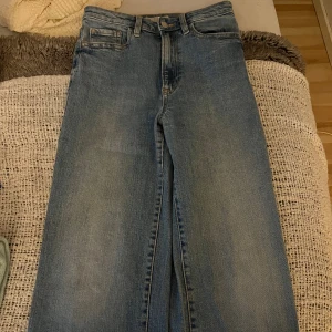 Blå raka jeans med hög midja - Snygga blå jeans med klassisk femficksdesign och hög midja. Jeansen har raka ben och en ljus tvätt som ger en avslappnad vibe. Perfekta att matcha med sneakers eller boots för en cool look.