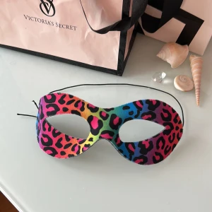 Färgglad leopardmask med svart baksida - Säljer en cool mask med leopardmönster i regnbågens färger på framsidan och svart tyg på baksidan. Masken har en smidig elastisk snodd för enkel användning och är perfekt för maskerad eller fest. Materialet känns mjukt och följsamt mot huden.