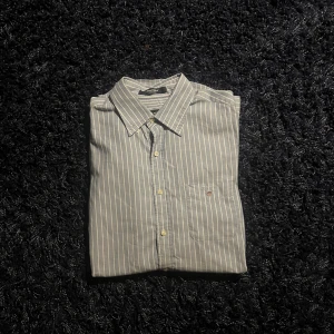 Randig skjorta från Gant, M - Snygg blå och vit randig skjorta från Gant i regular fit. Klassisk krage, knäppning framtill och liten bröstficka med Gant-logga. Perfekt för dig som gillar stilrena och tidlösa plagg.